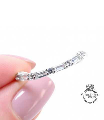 A close-up image of a person's hand holding a silver ring with a row of small diamonds along the band.