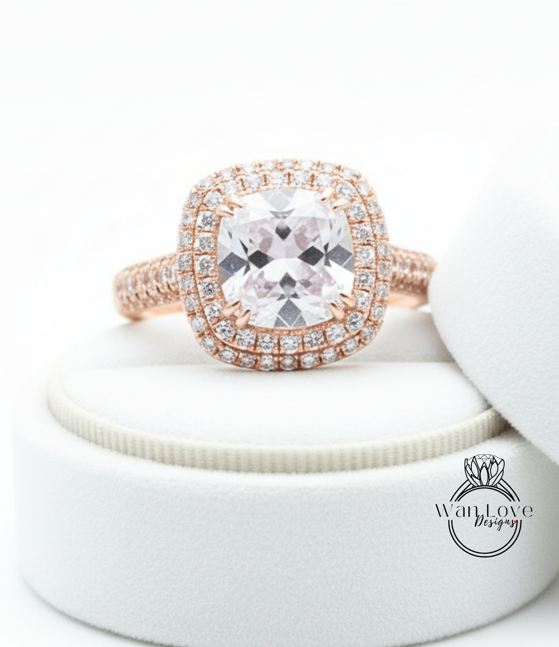 A large, clear gemstone ring with a halo of smaller diamonds around the center stone, displayed on a white velvet cushion.