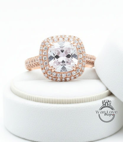 A large, clear gemstone ring with a halo of smaller diamonds around the center stone, displayed on a white velvet cushion.