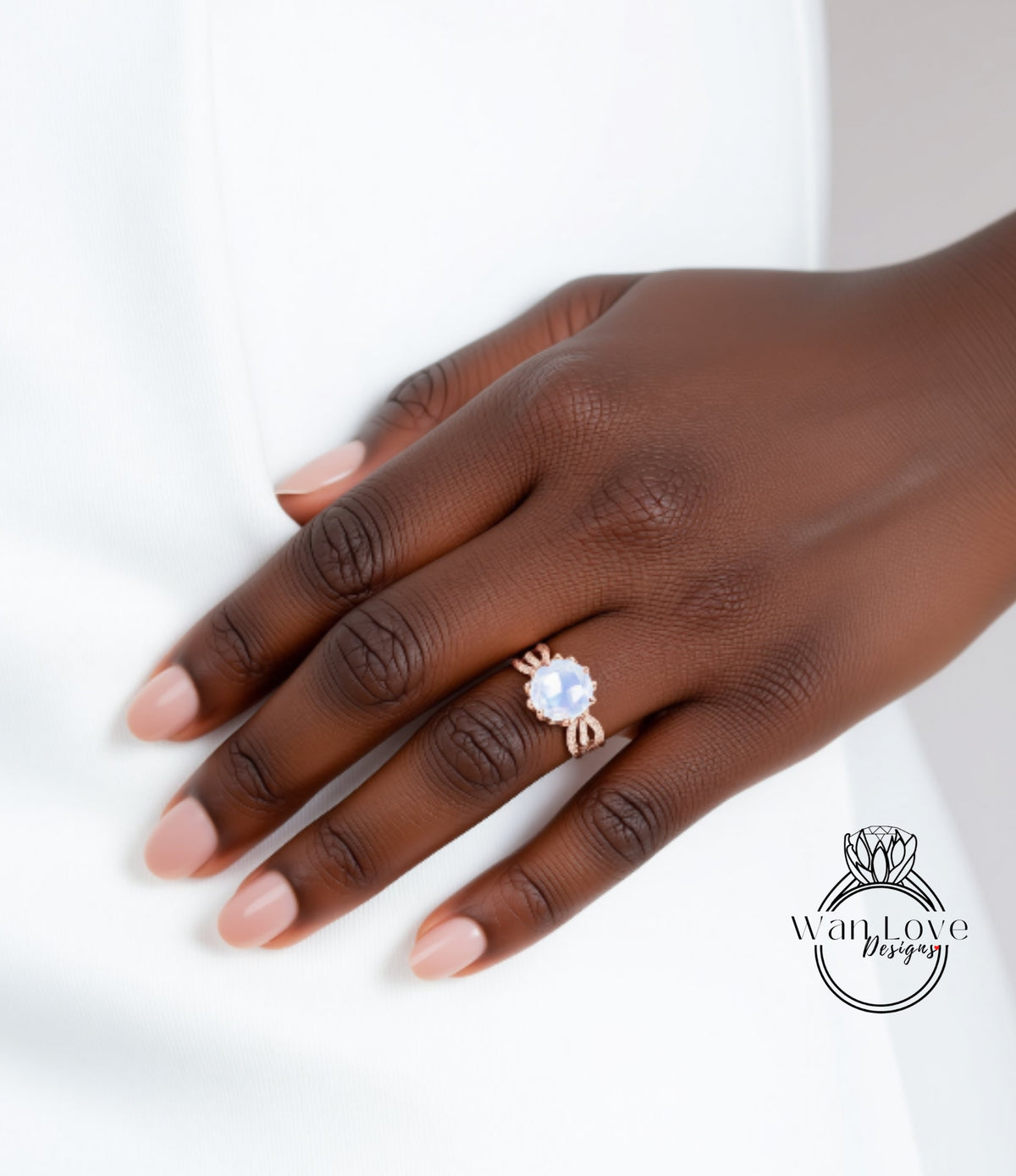 A close-up of a hand wearing a ring with a large gemstone, resting on a white surface.