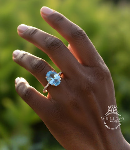 A close-up of a hand wearing a large blue gemstone ring against a blurred green background.