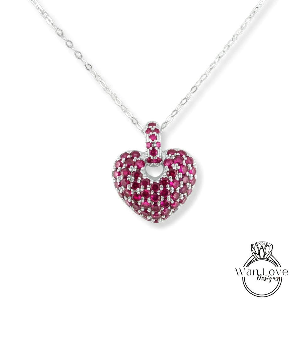 A heart-shaped pendant necklace with a large, sparkling red gemstone in the center.