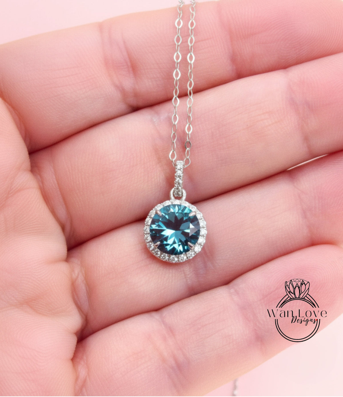 A hand holding a silver necklace with a blue gemstone pendant.