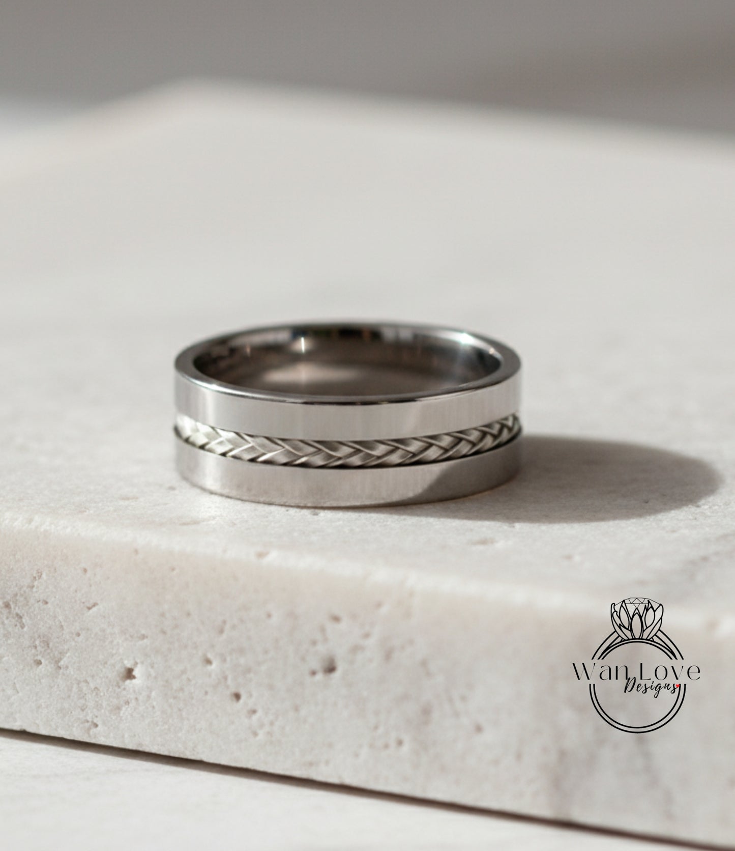 A silver ring with a braided band is displayed on a white surface.