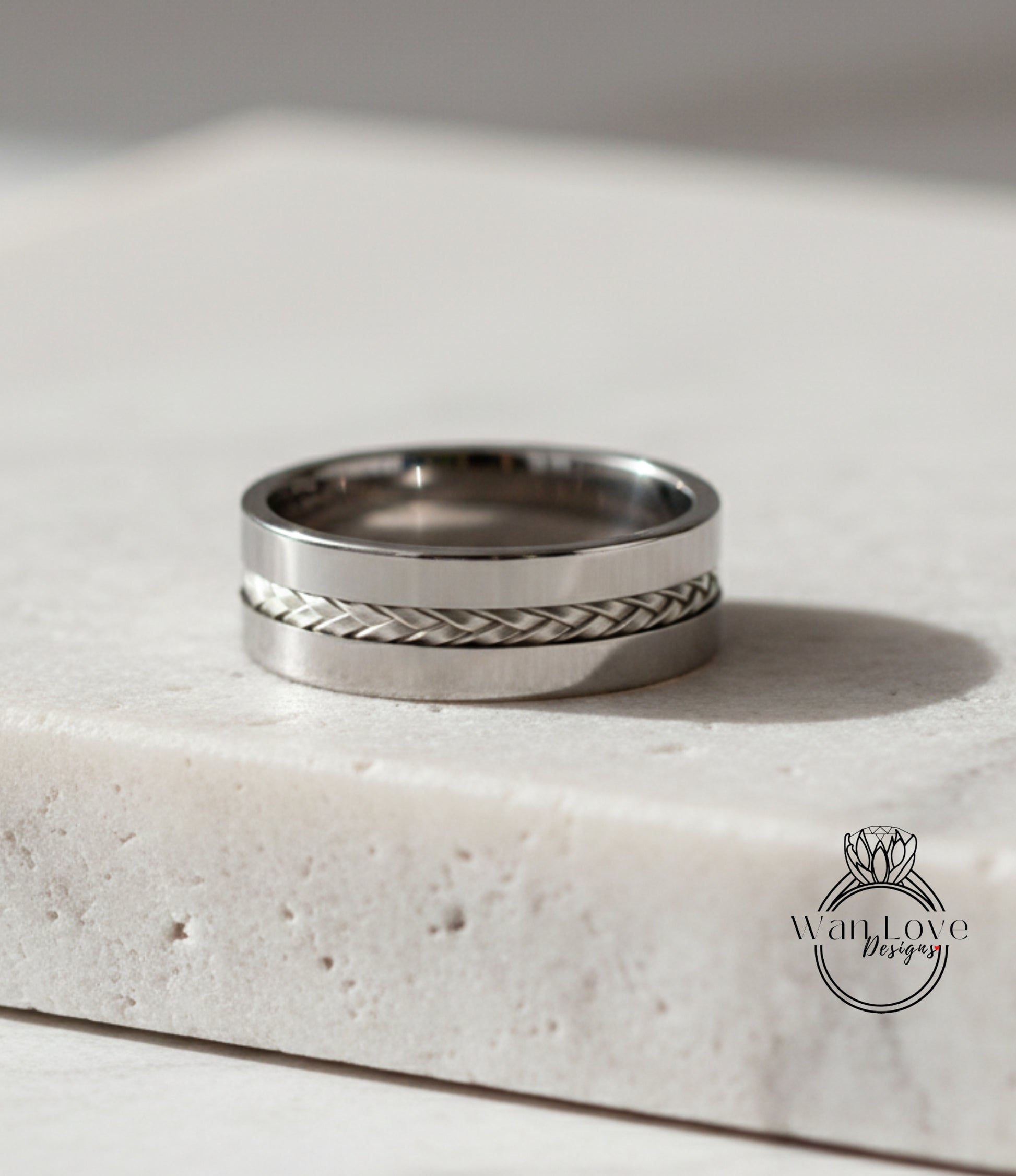 A silver ring with a braided band is displayed on a white surface.