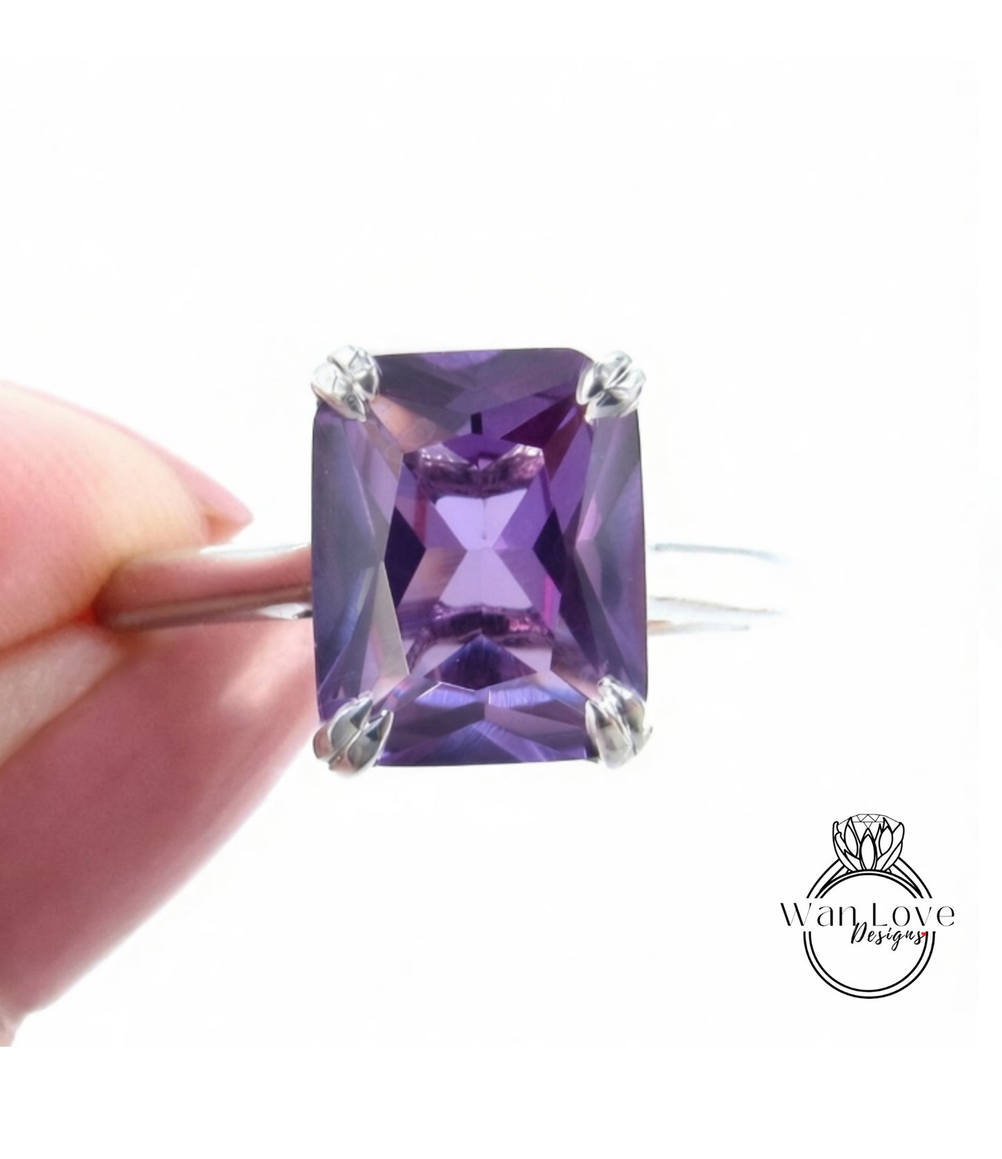 A hand holding a ring with a large, purple gemstone, likely an amethyst, against a white background.