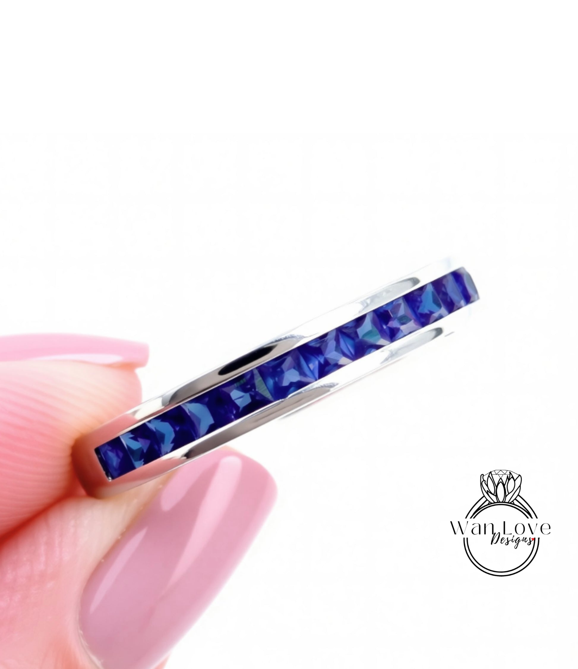 A close-up image of a person's hand holding a silver ring with a row of blue gemstones.