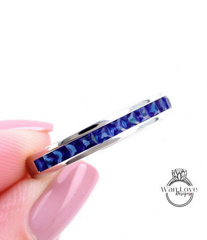 A close-up image of a person's hand holding a silver ring with a row of blue gemstones.