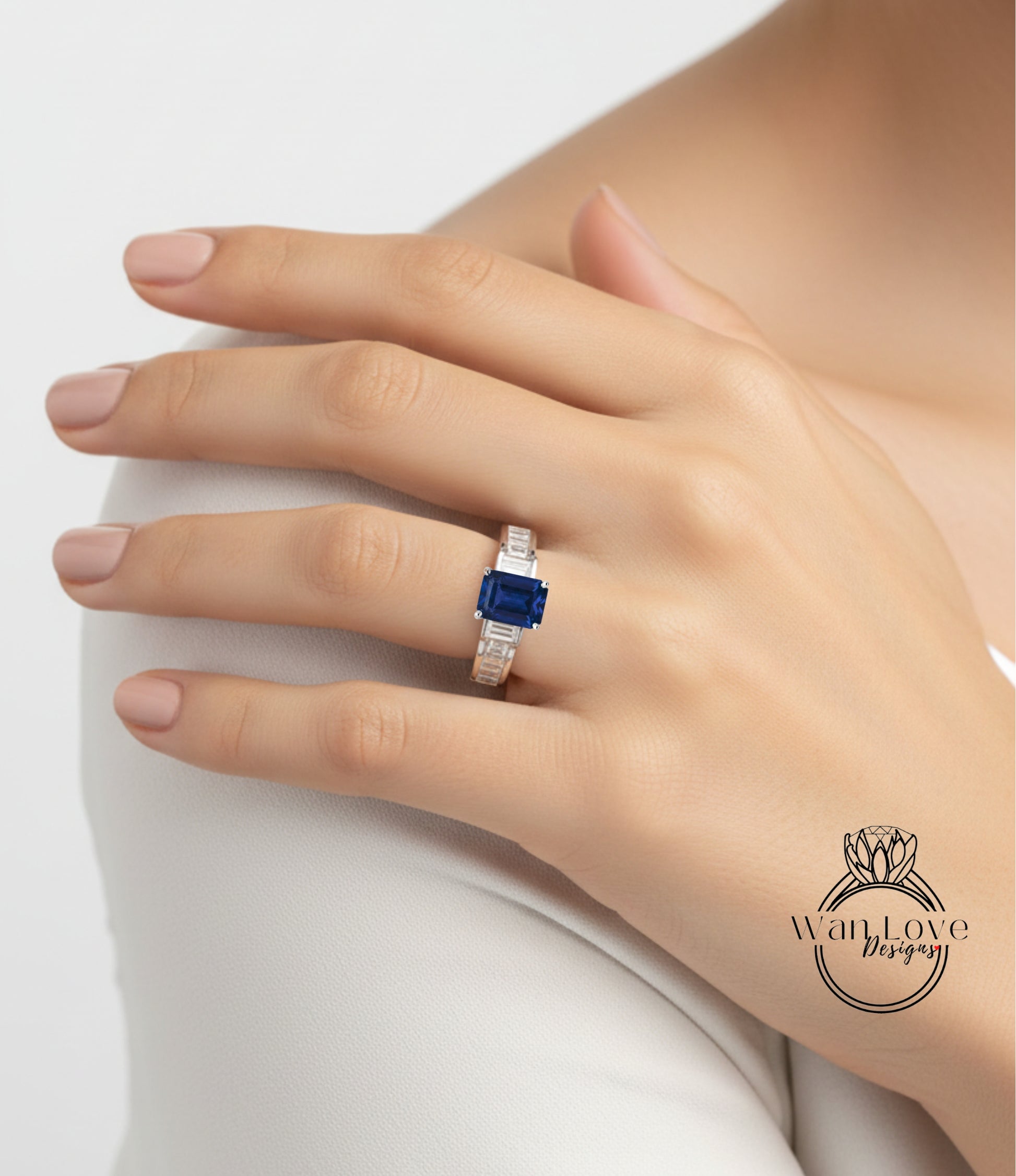 A close-up of a person's hand wearing a ring with a blue gemstone, resting on a white surface.
