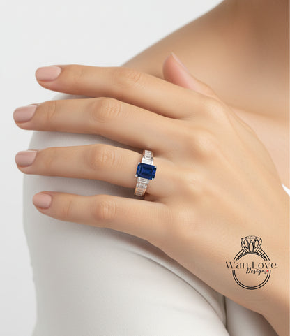 A close-up of a person's hand wearing a ring with a blue gemstone, resting on a white surface.