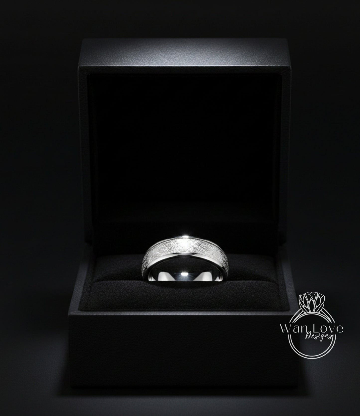 A silver ring is displayed in a black jewelry box against a dark background.