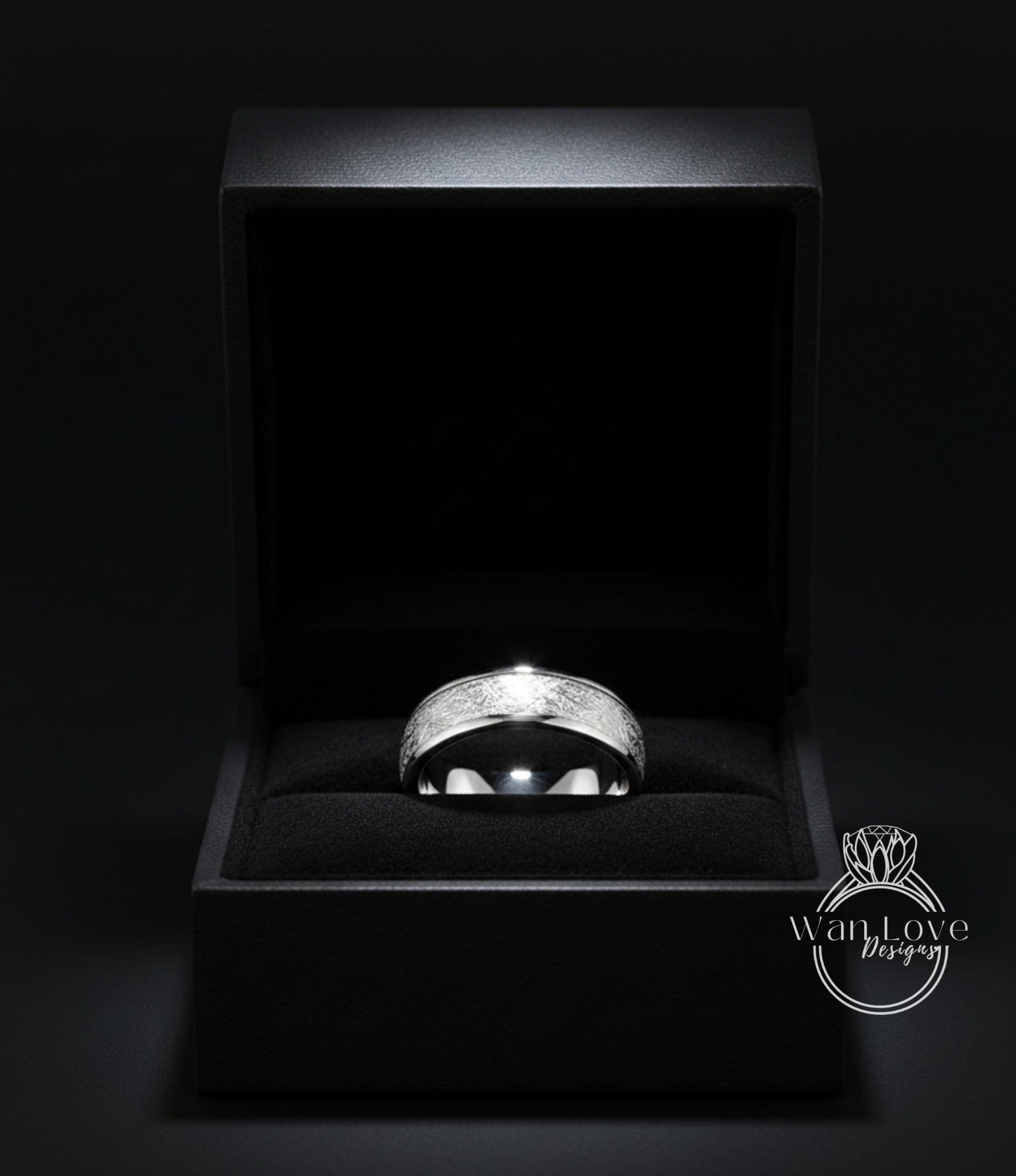 A silver ring is displayed in a black jewelry box against a dark background.