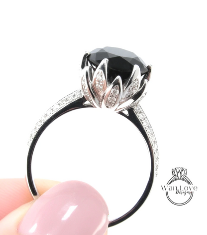 A close-up of a person's hand holding a silver ring with a large black gemstone, likely a diamond, and a decorative flower-like element.