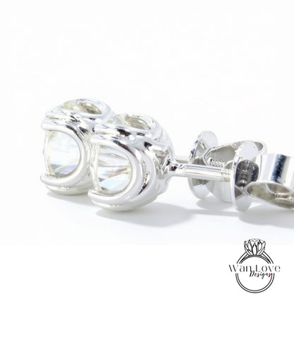 A pair of silver earrings with a clear gemstone, resting on a white surface.