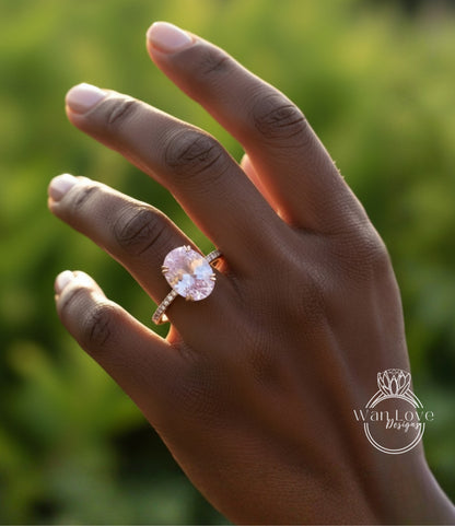 A close-up of a hand wearing a pink diamond engagement ring against a blurred green background.