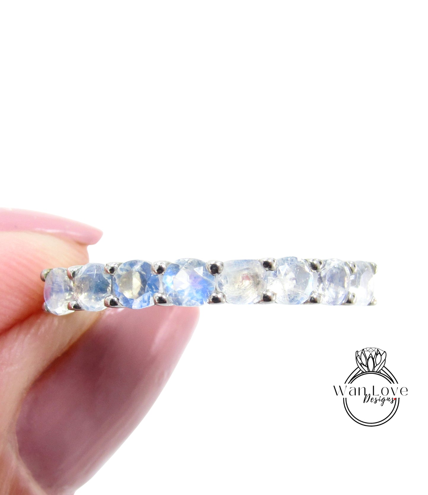 A hand holding a ring with a row of blue moonstone gemstones.