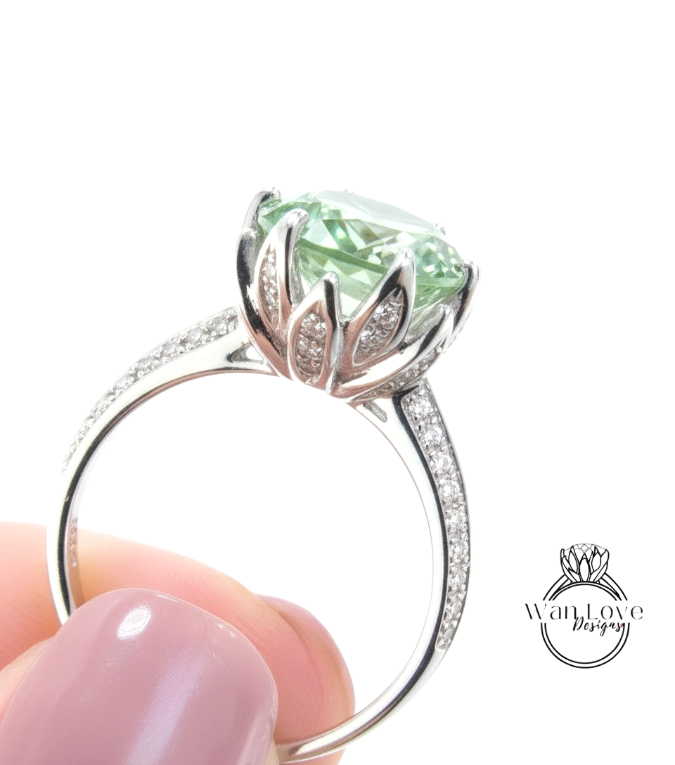 A close-up of a silver ring with a large, green gemstone, possibly a diamond, set in a decorative flower-like design.