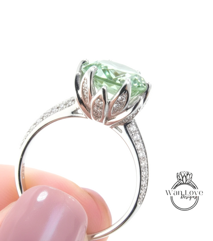 A close-up of a silver ring with a large, green gemstone, possibly a diamond, set in a decorative flower-like design.