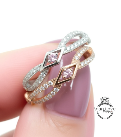 A close-up of a person's hand wearing a ring with two diamond-encrusted bands, one silver and one gold, with a pink gemstone in the center.
