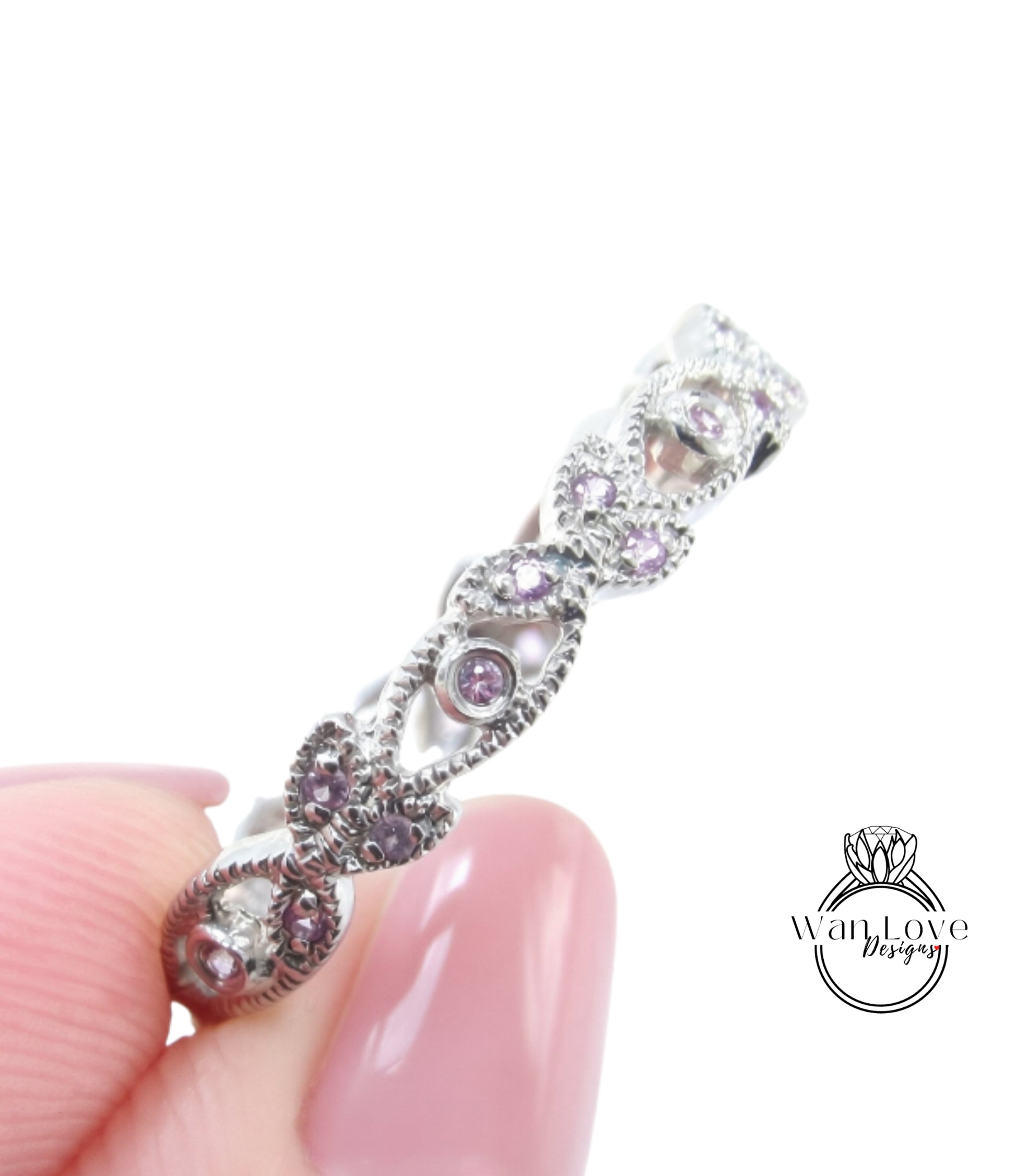A close-up image of a person's hand holding a silver ring adorned with small purple gemstones.