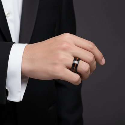 A close-up of a person's hand wearing a black and orange ring against a dark background.