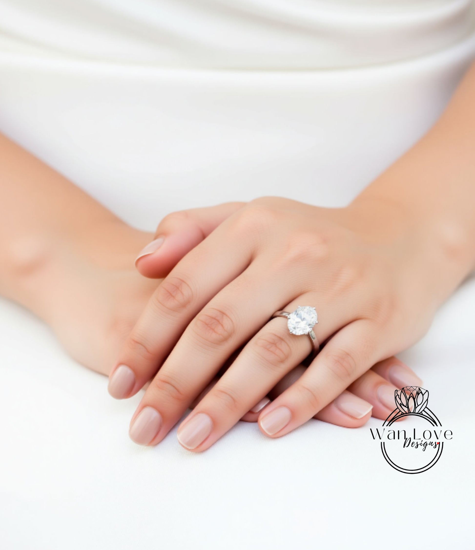 A close-up of a person's hands resting on a white surface, with a large diamond engagement ring visible on one of the fingers.