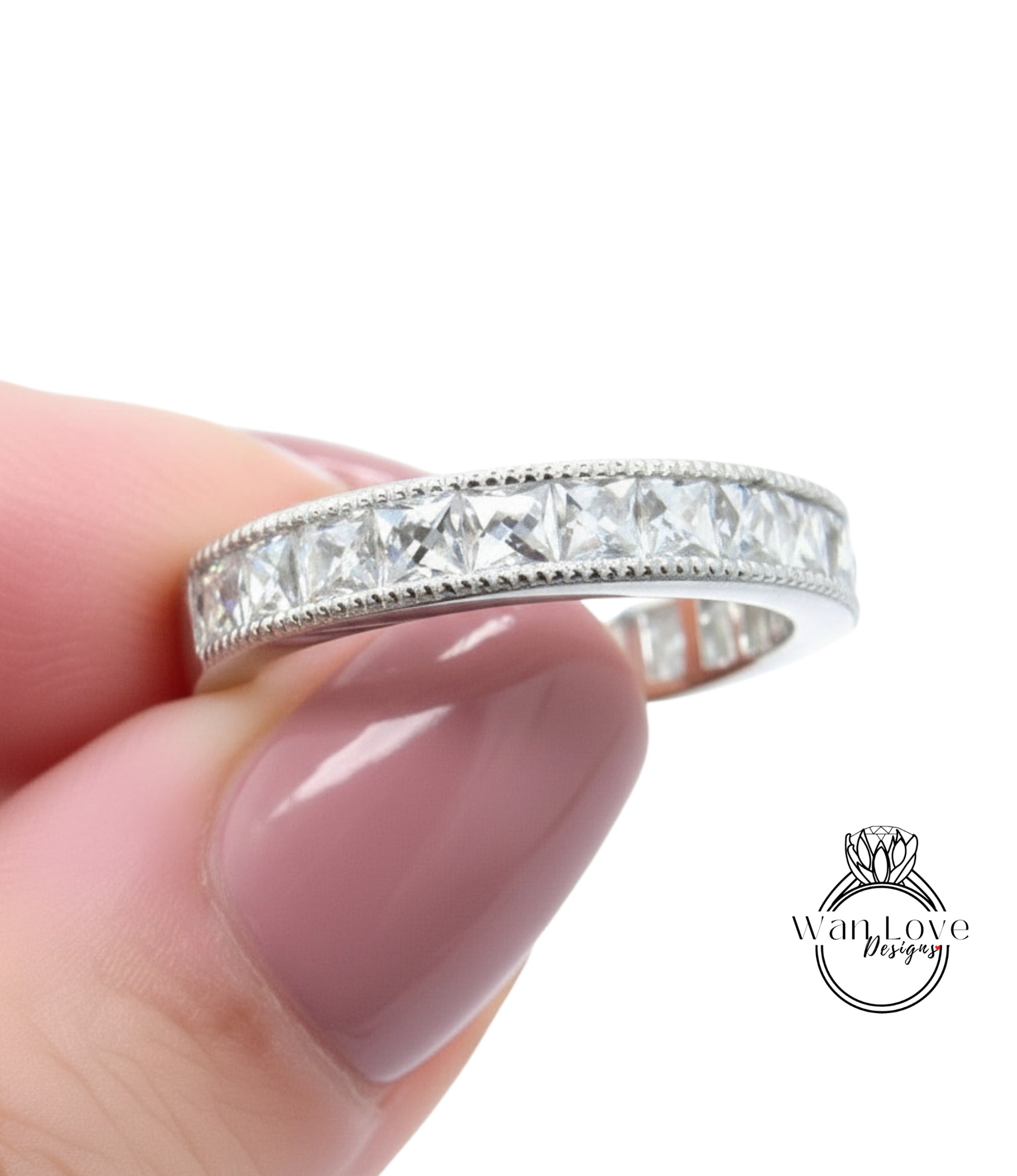 A close-up image of a person's hand holding a silver ring with a row of small diamonds along the band.
