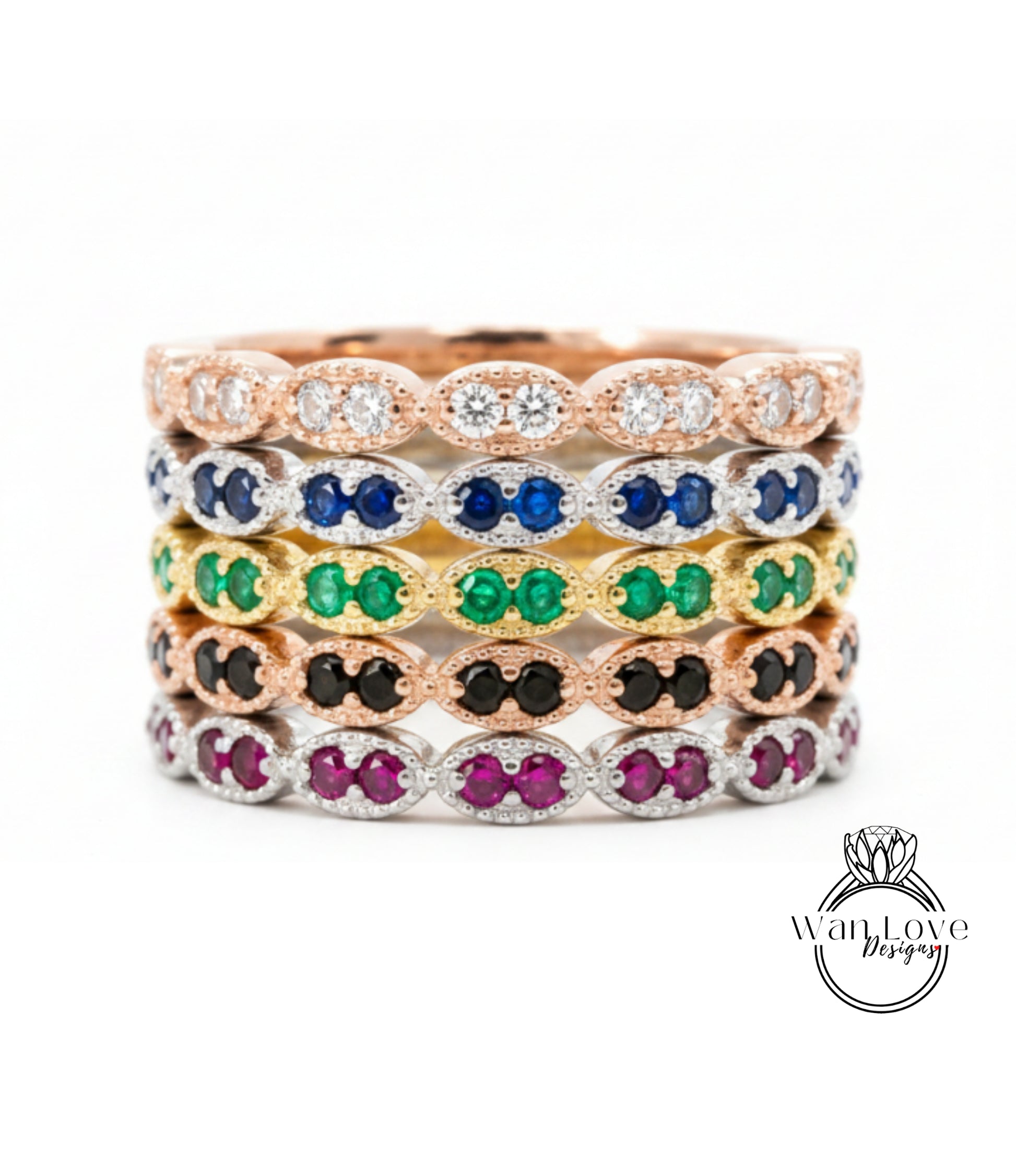 A stack of rings with various colored gemstones, including diamonds and emeralds, set in a rose gold or silver tone.