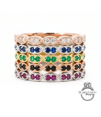 A stack of rings with various colored gemstones, including diamonds and emeralds, set in a rose gold or silver tone.