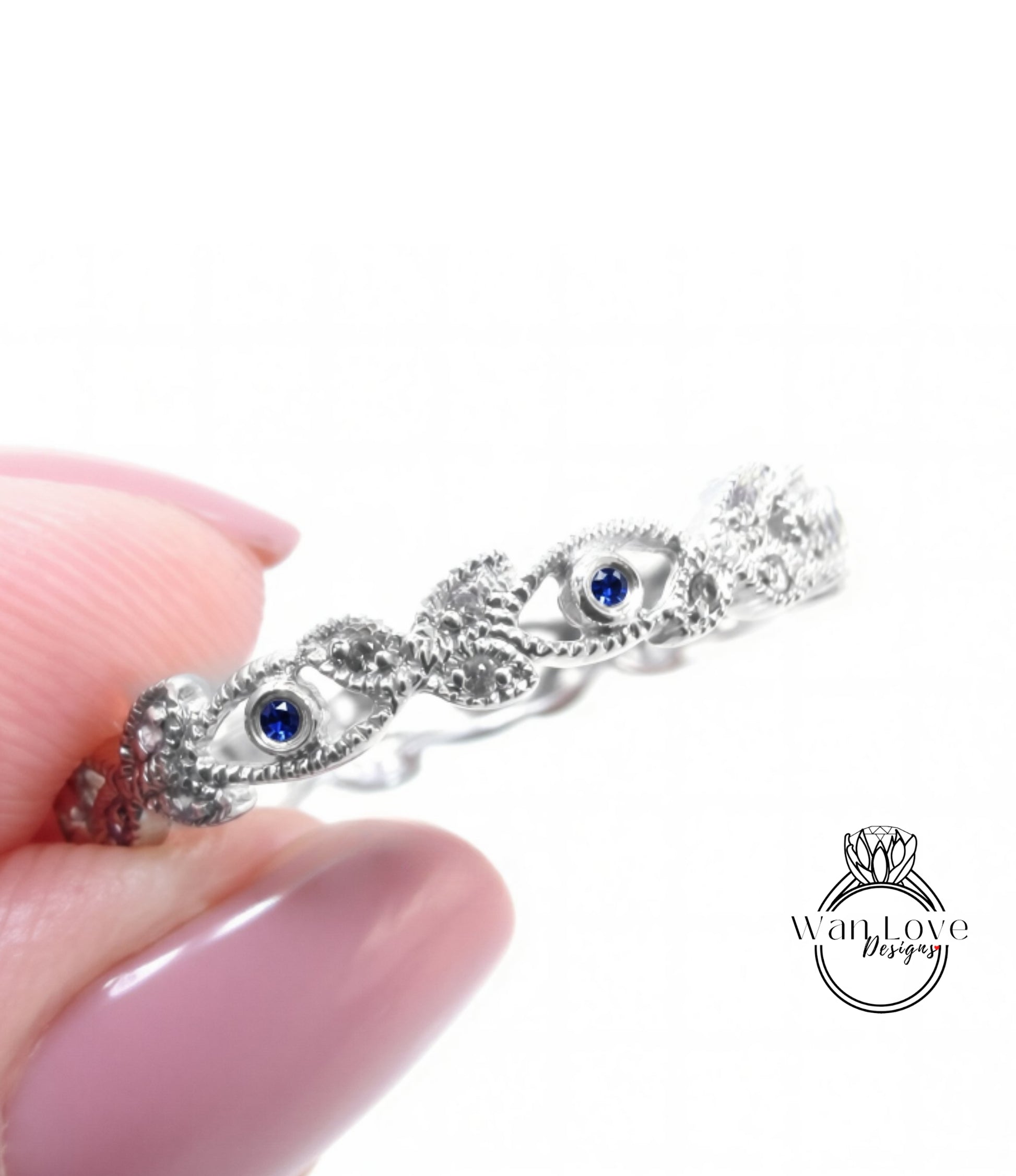 A close-up image of a person's hand holding a silver ring with blue gemstones.