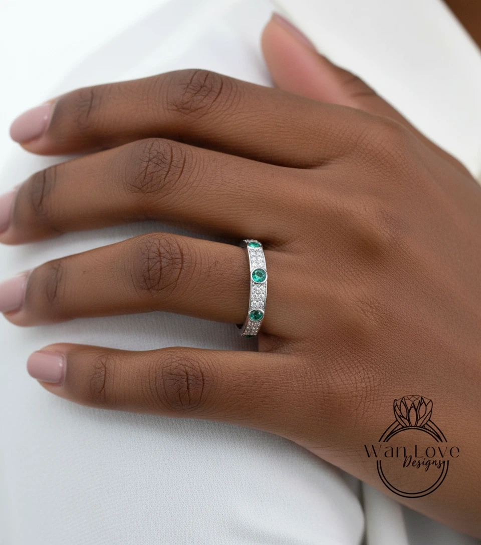 A close-up of a person's hand wearing a silver ring with green gemstones.