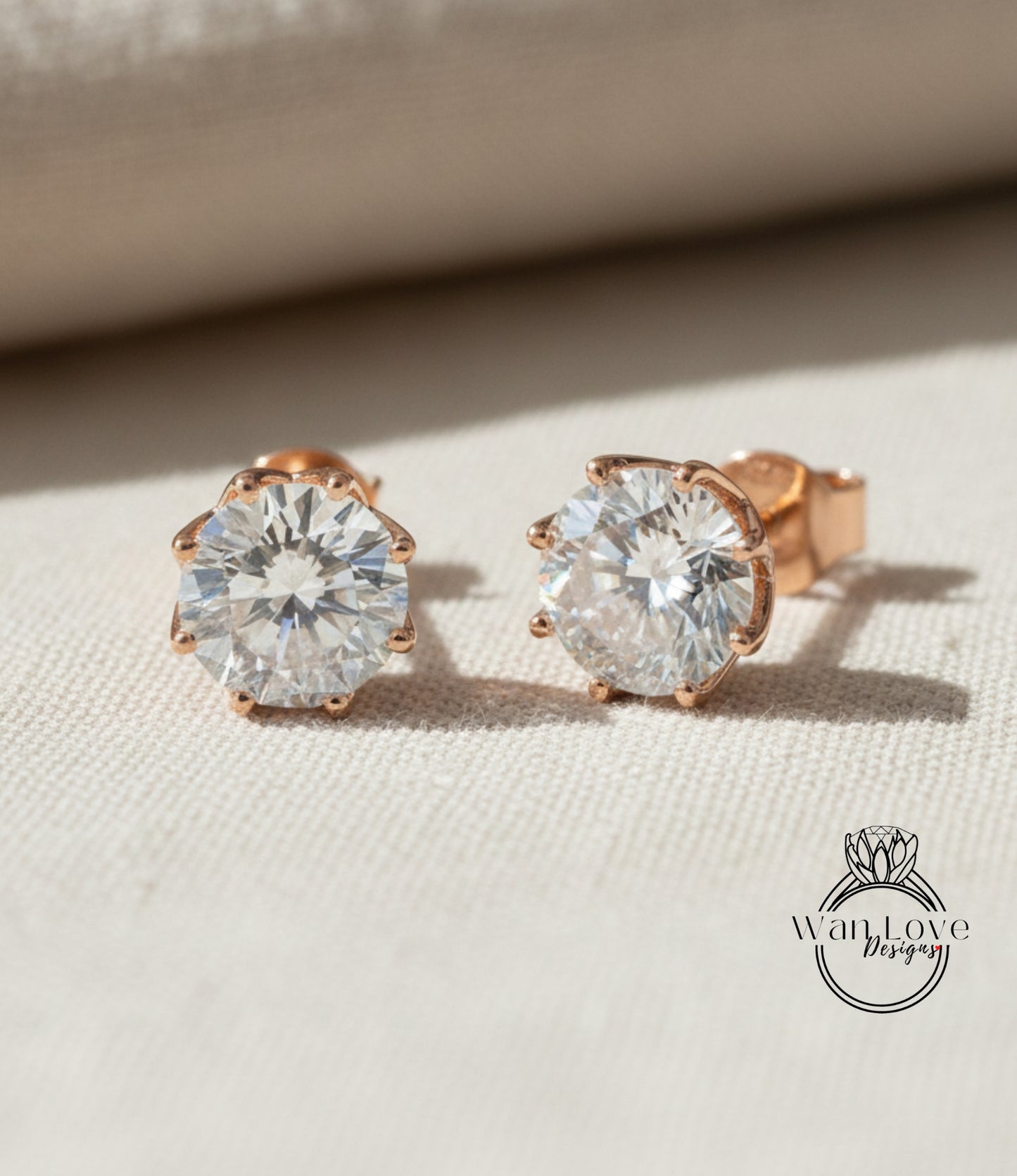 A pair of elegant diamond earrings with a large central diamond surrounded by smaller diamonds, resting on a beige fabric background.