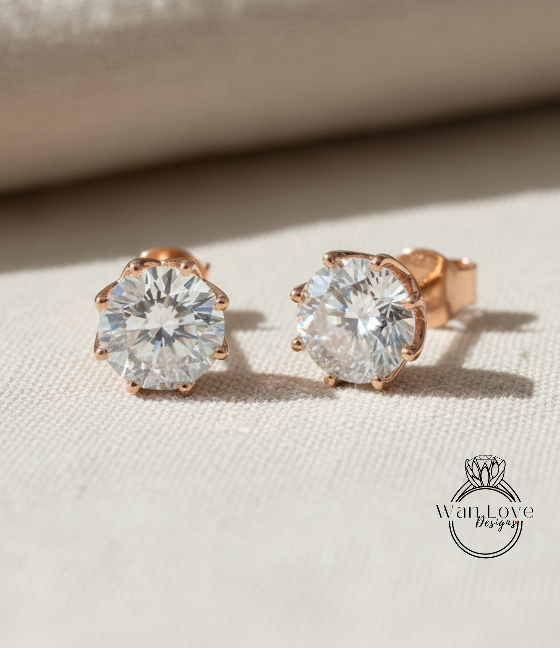 A pair of elegant diamond earrings with a large central diamond surrounded by smaller diamonds, resting on a beige fabric background.