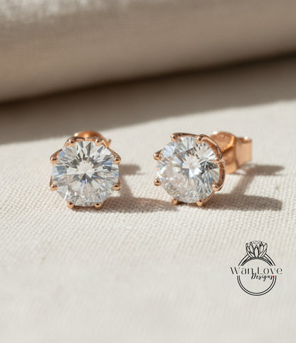 A pair of elegant diamond earrings with a large central diamond surrounded by smaller diamonds, resting on a beige fabric background.