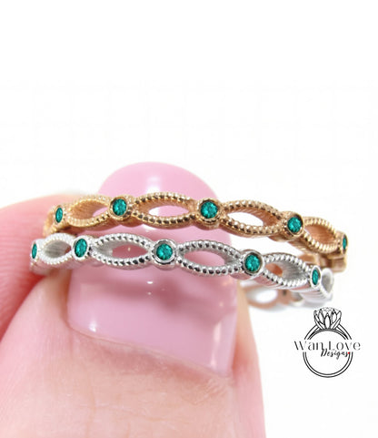A close-up of a person's hand holding a ring with a decorative band and green gemstones.