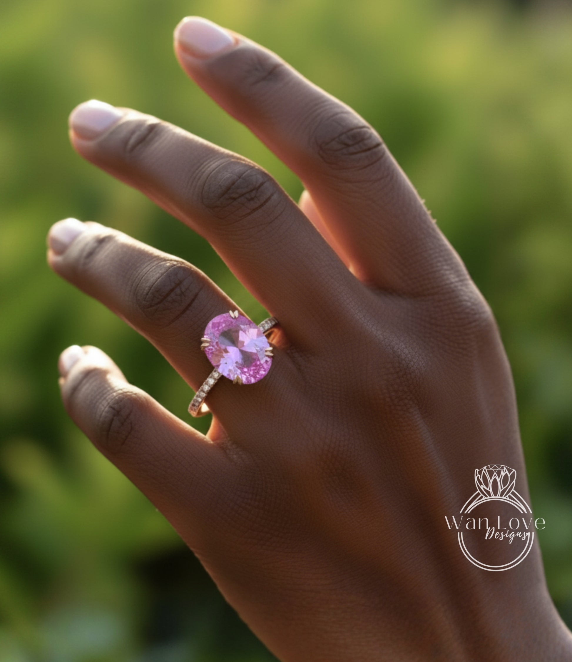 A close-up of a person's hand wearing a pink gemstone ring against a blurred green background.