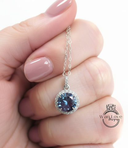 A hand holding a silver necklace with a blue gemstone pendant.