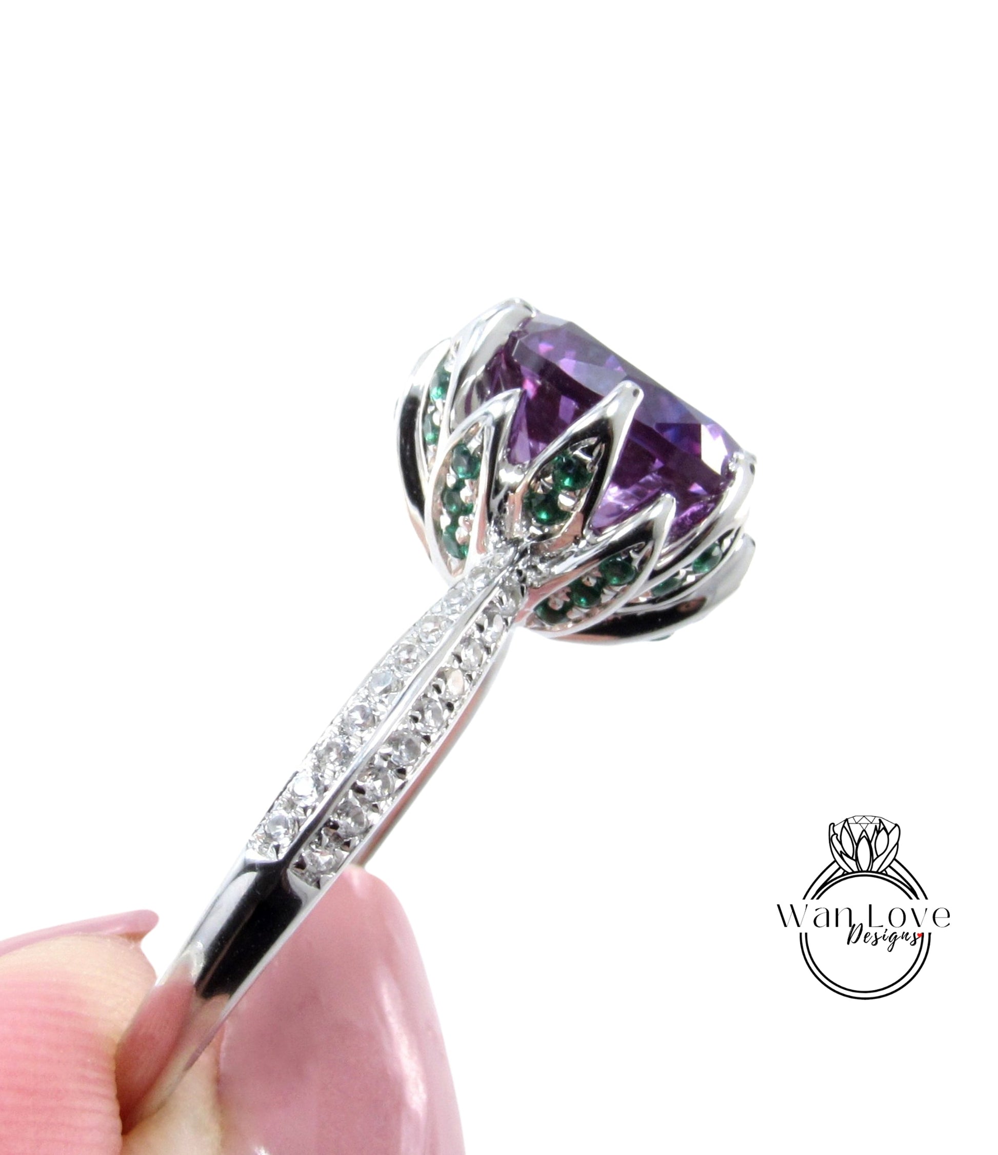 A close-up view of a silver ring with a large purple gemstone, possibly a diamond, and green gemstones.