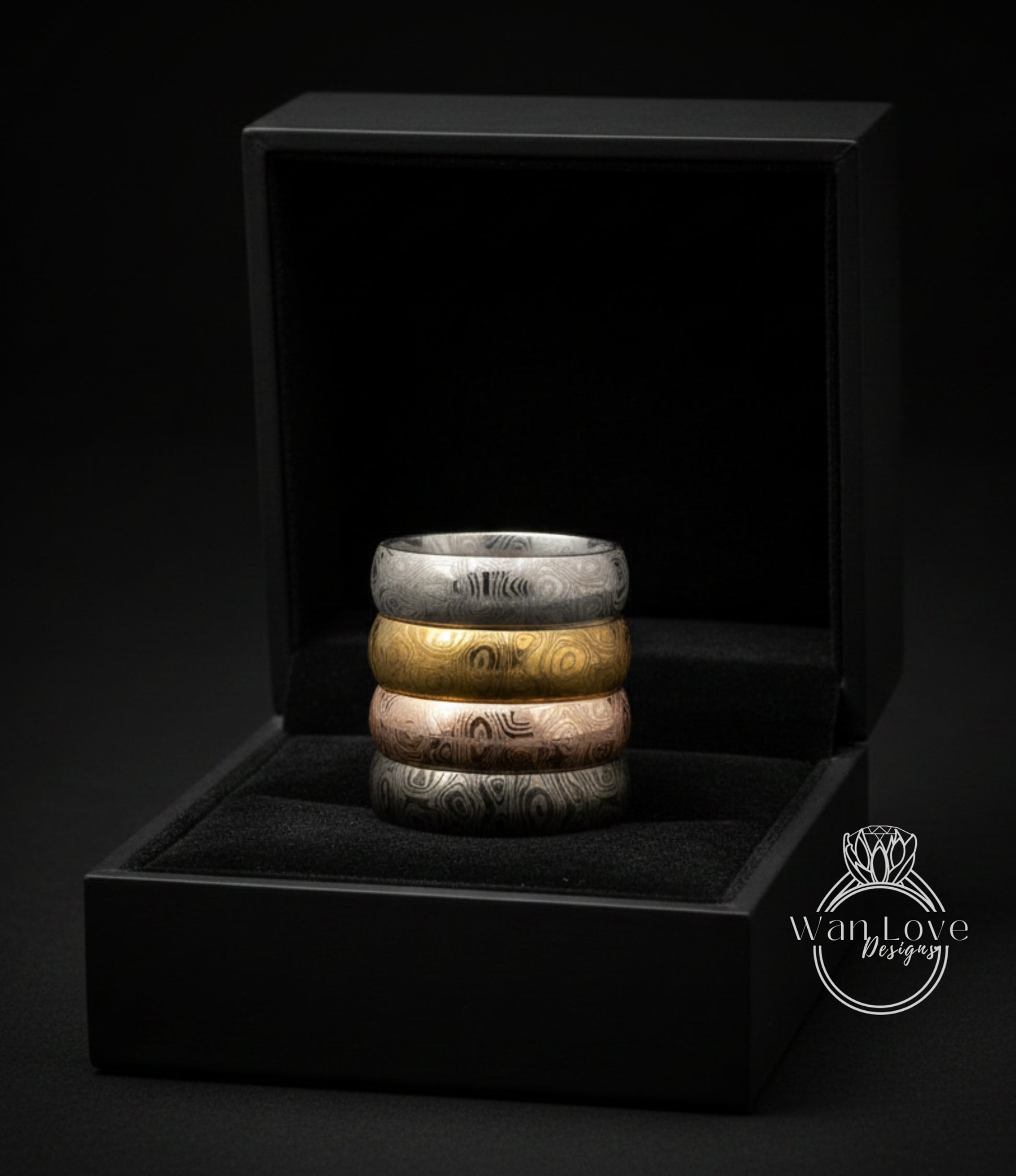 A black jewelry box containing a stack of rings in various colors, including silver, gold, and bronze.