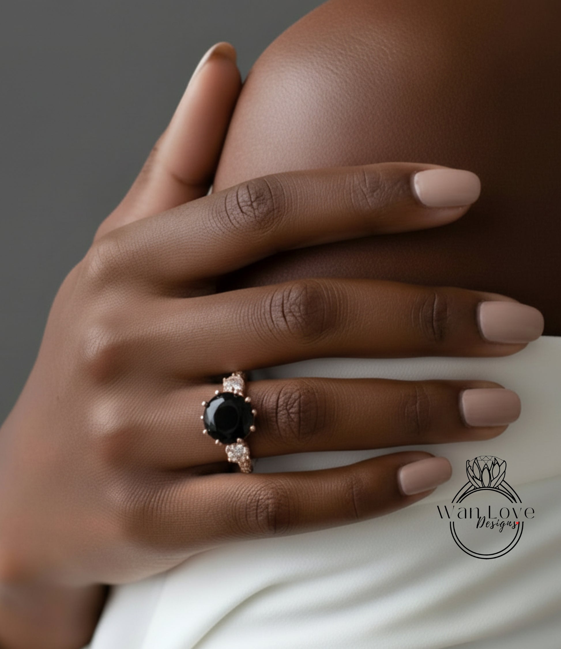 A close-up of a hand wearing a ring with a large black gemstone, resting on a white fabric.
