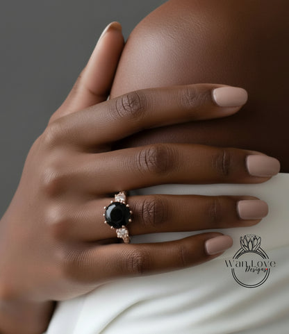 A close-up of a hand wearing a ring with a large black gemstone, resting on a white fabric.
