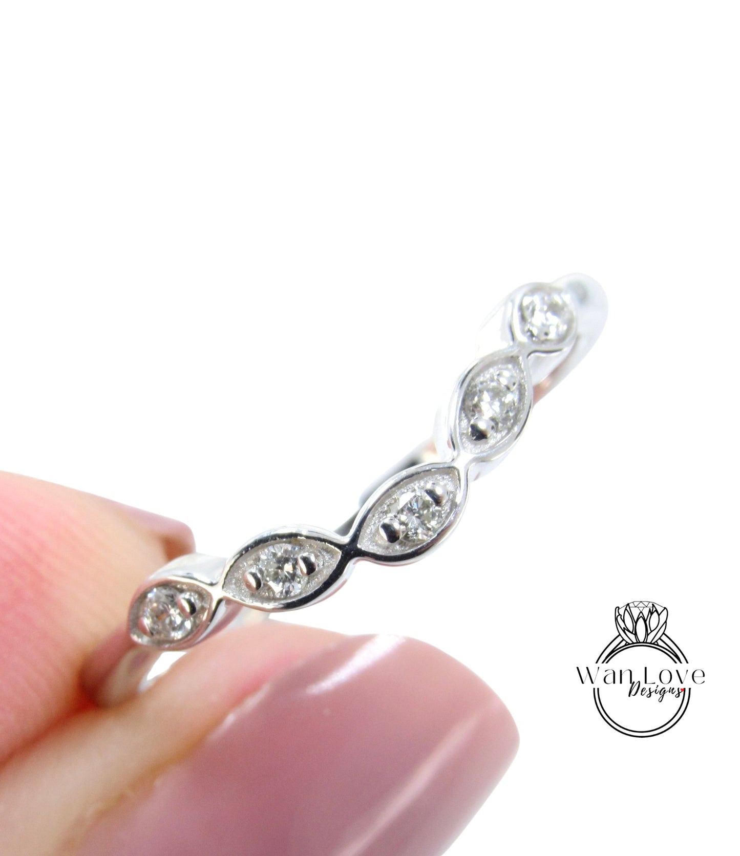 A close-up image of a person's hand holding a silver ring with a row of small diamonds on it.