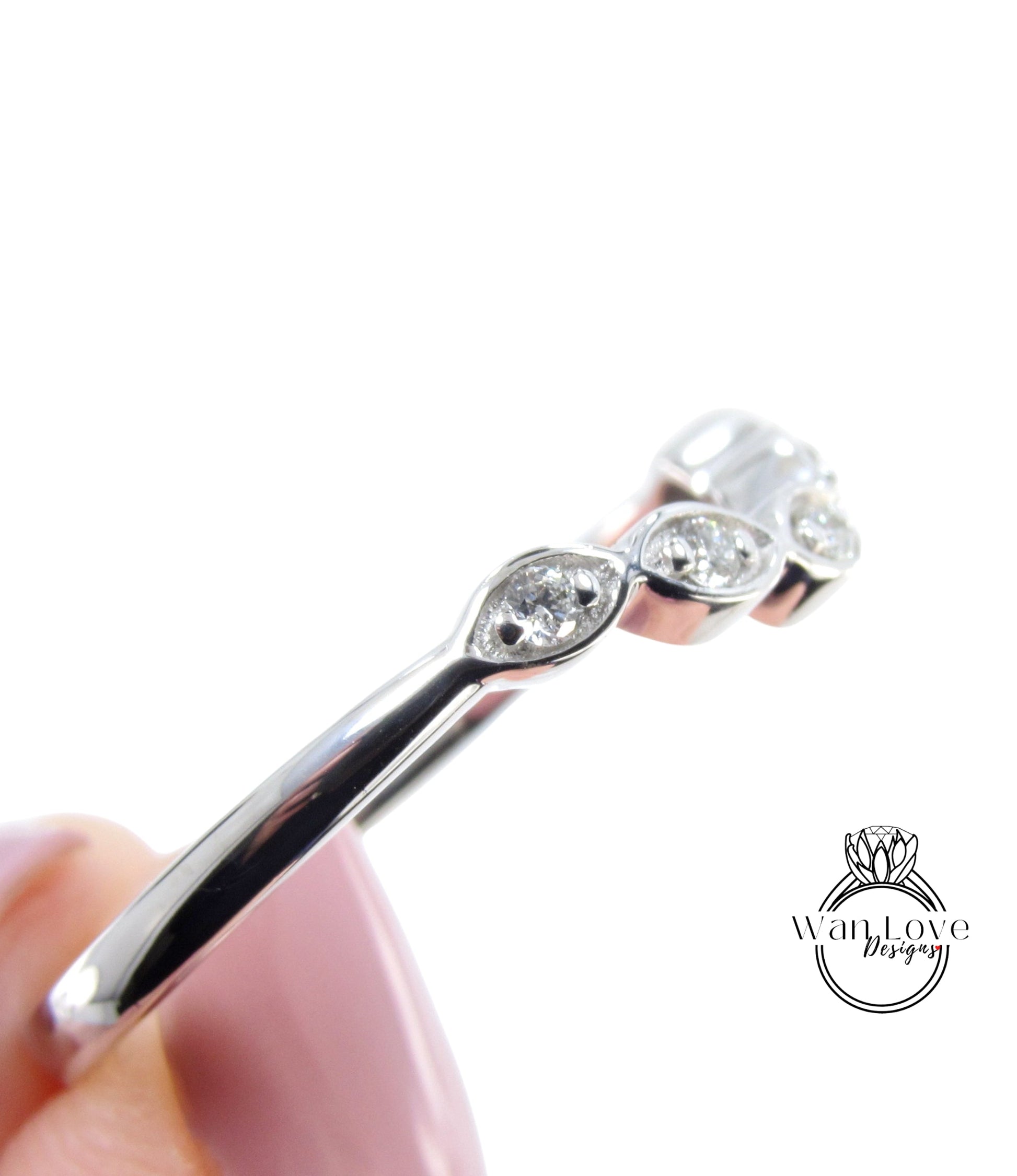 A close-up view of a silver ring with a row of small diamonds set in it, held in a hand against a white background.