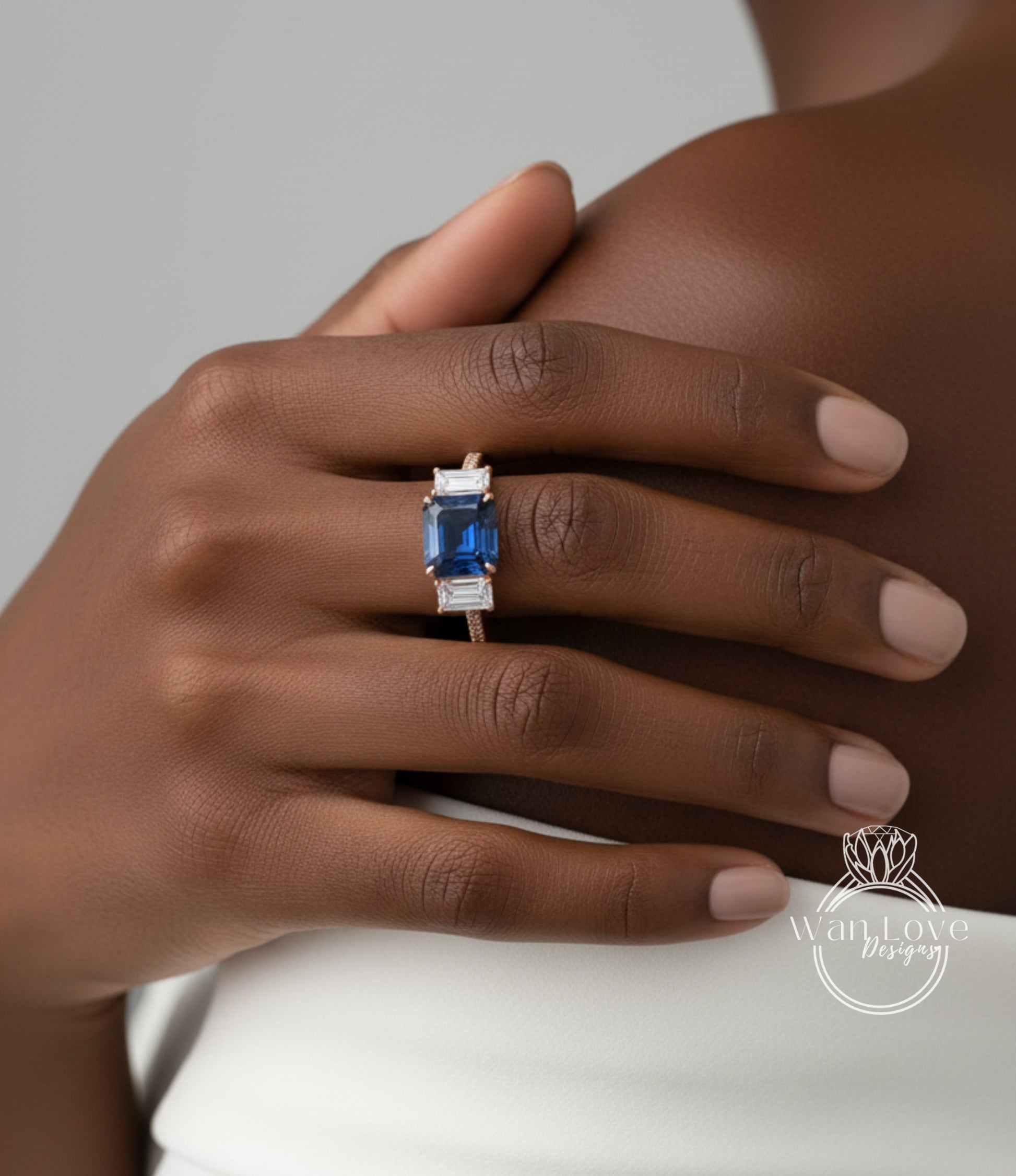 A close-up of a person's hand wearing a ring with a blue gemstone, resting on the shoulder of another person.