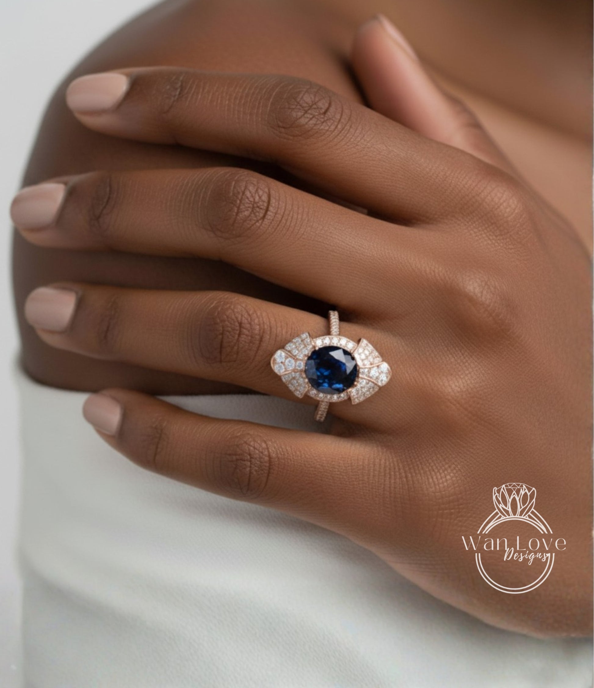 A close-up of a hand wearing a ring with a large blue gemstone, resting on a white fabric.