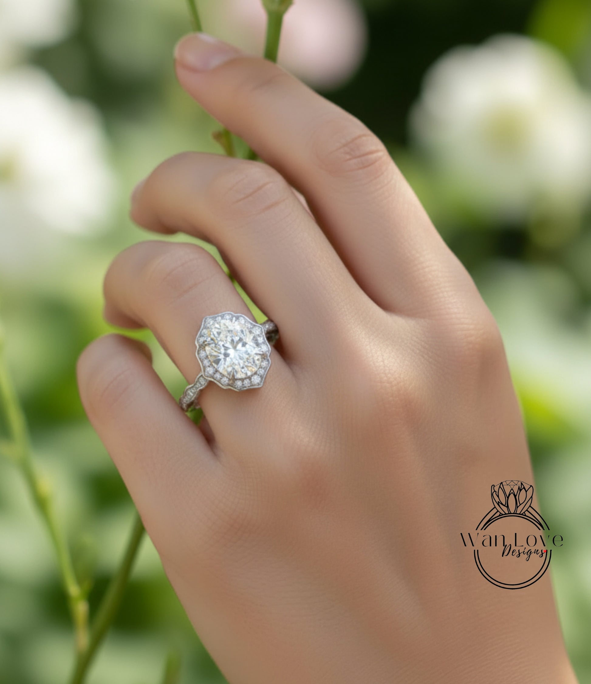 A close-up of a hand wearing a diamond engagement ring, with a blurred background of greenery.