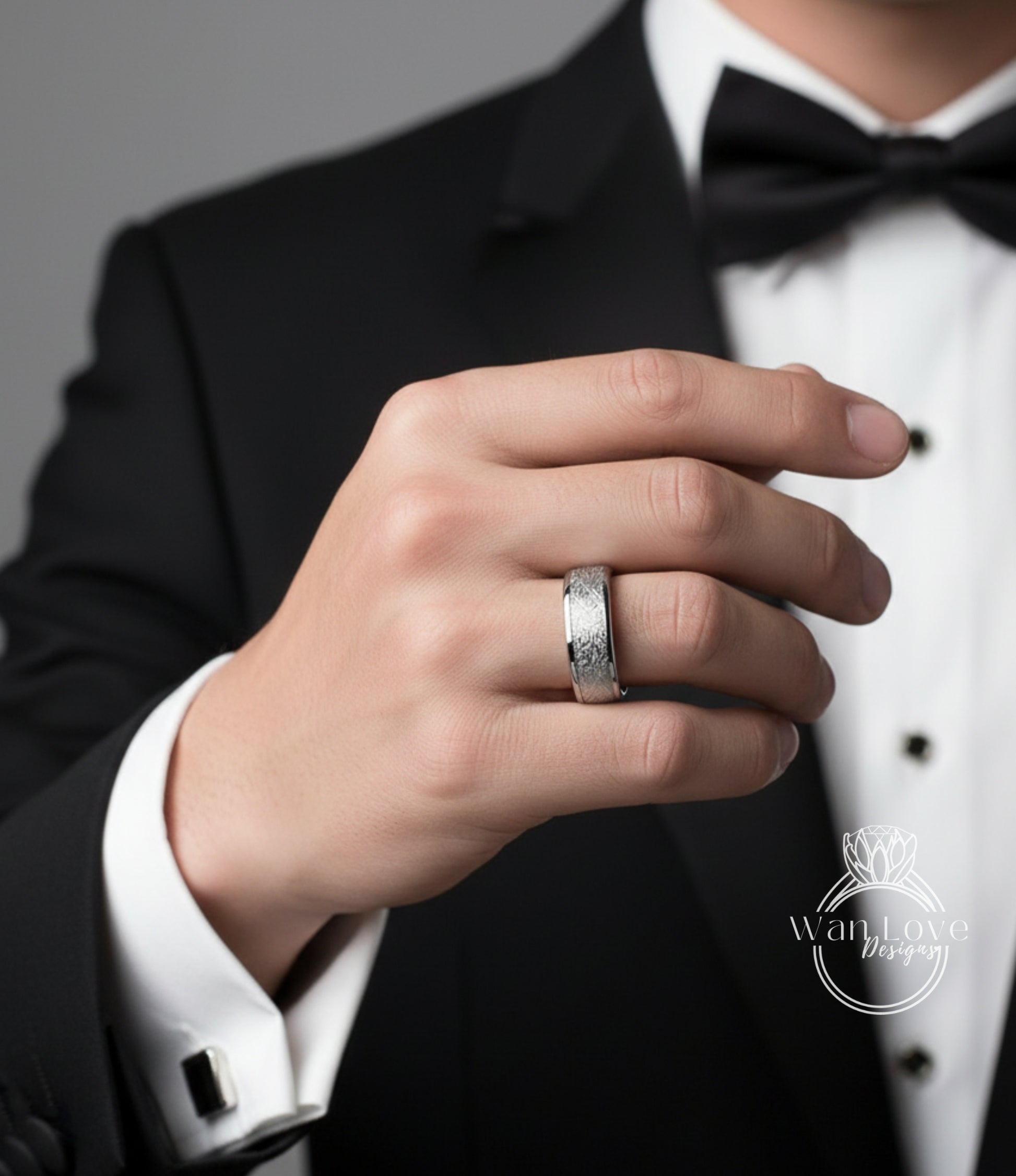A close-up of a person's hand wearing a silver ring, with a black bow tie visible.