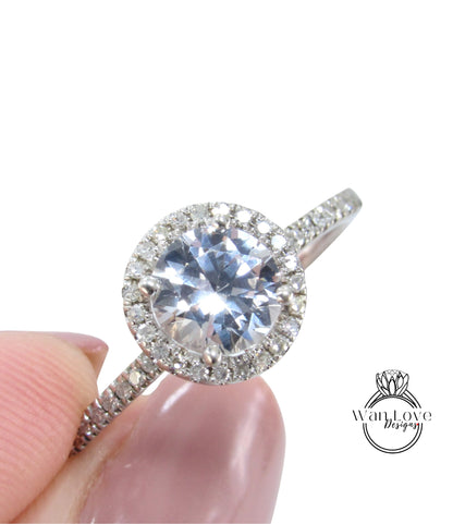 A close-up image of a diamond engagement ring being held in someone's hand, showcasing the sparkling center stone surrounded by a halo of smaller diamonds.
