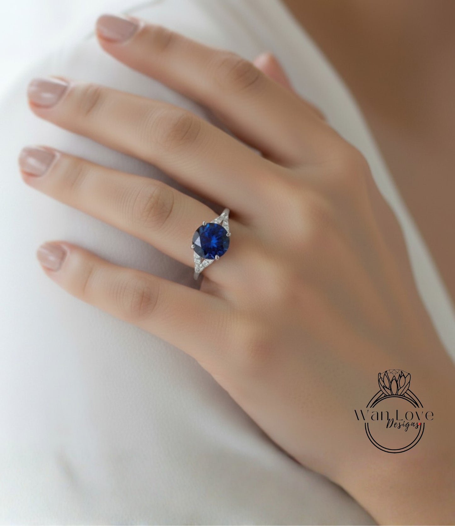 A close-up of a hand wearing a ring with a large blue gemstone, resting on a white surface.