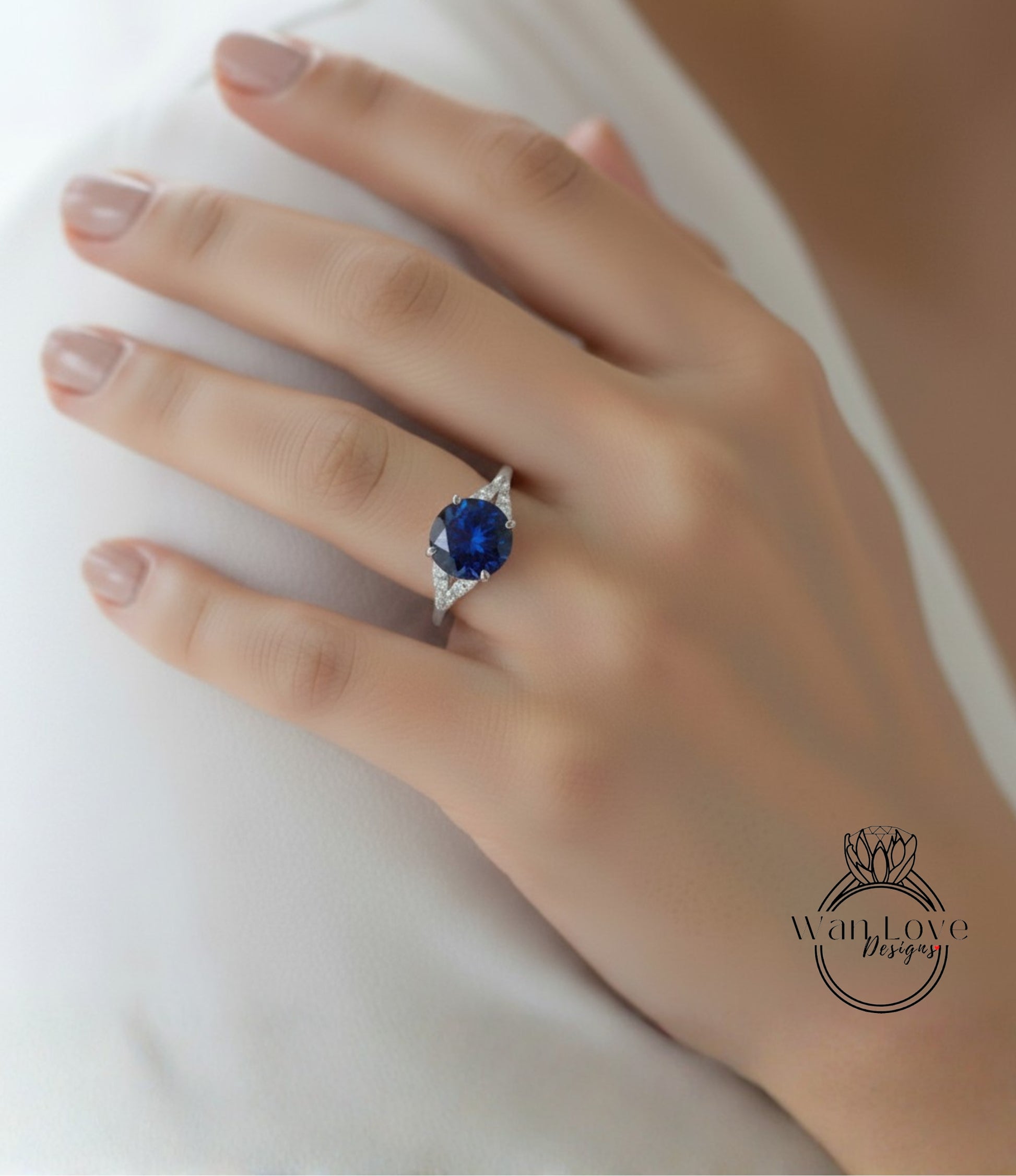 A close-up of a hand wearing a ring with a large blue gemstone, resting on a white surface.